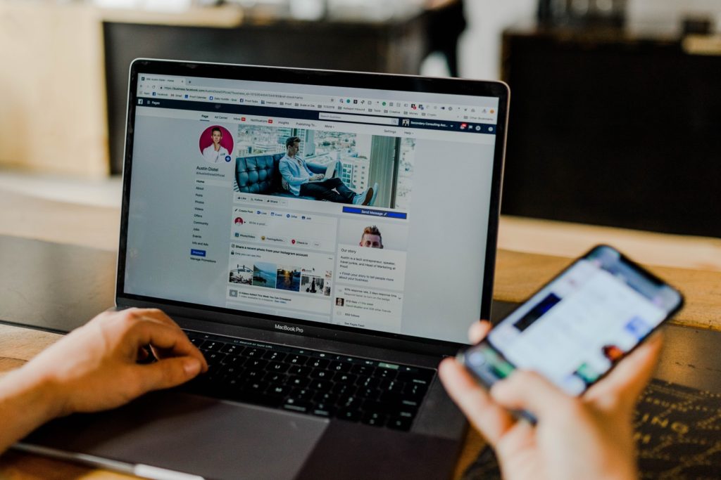 A person using a mobile phone and laptop simultaneously on Facebook